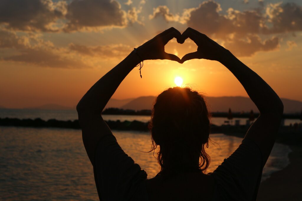 Katrina vor untergehender Sonne am Meer der Toskana/Italia die Hände zum Herzen geformt über den Kopf haltend