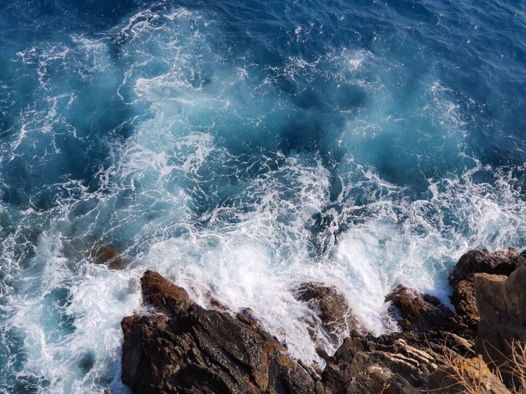 Blaues Meer mit weißer Gischt an Felsen von oben 