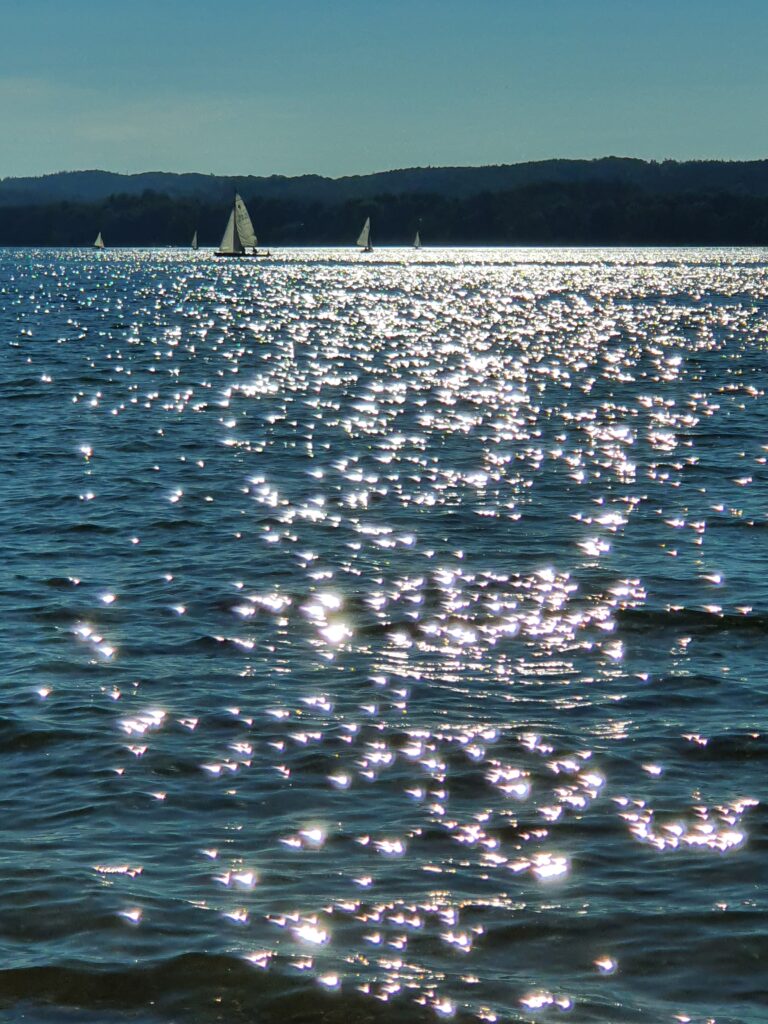 Starnberger See mit funkelndem Wasser, im Hintergrund weiße Segelboote